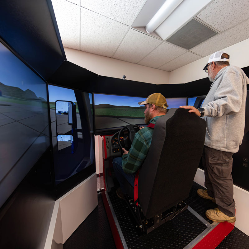 photo of a student using the CDL simulator with an instructor standing beside