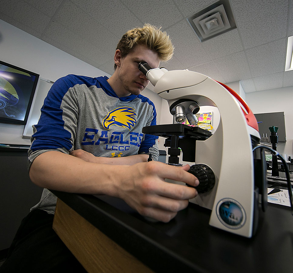 photo of male student looking into a microscope in the biology classroom.