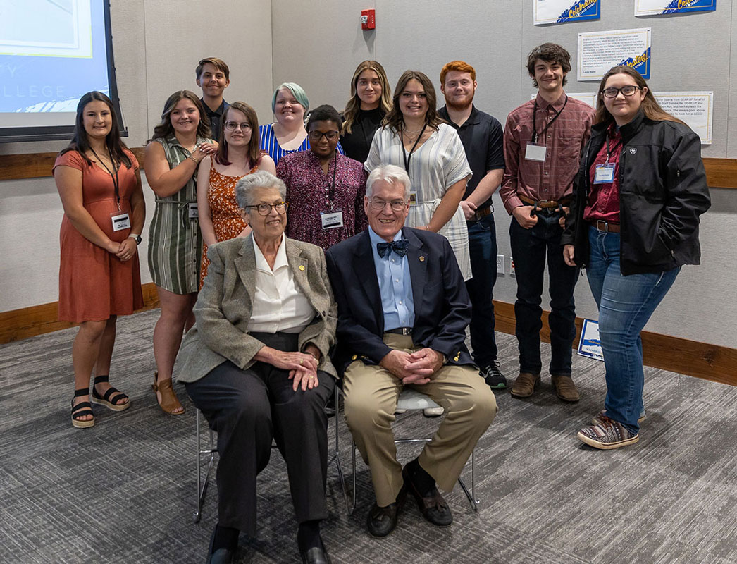 photo of 11 students lined up in the background who participated in the Davis First Generation Experience with Claire and Bud Davis sitting in chairs in front.