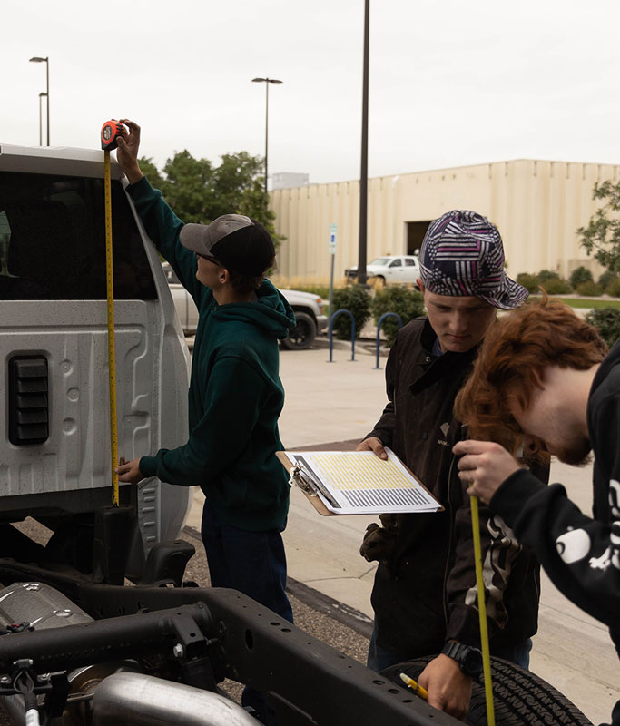 photo of students measuring and holding a clipboard near a truck that will be turned into the mobile welding lab.