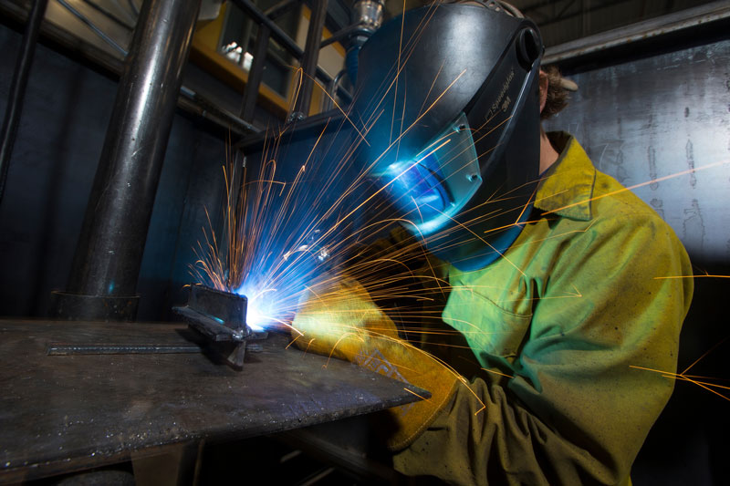 student in welding helmet welding with sparks flying