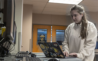 photo of a female student on a laptop in front of a row of computers in a classroom at LCCC.