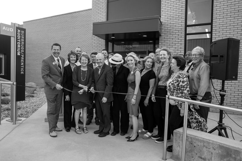 photo of the ribbon cutting for LCCC’s newest building, the Surbrugg Prentice Auditorium. Named in honor of Dr. Sandra Surbrugg and Dr. Robert Prentice. There is a large group of people in front of the building doors. Three are cutting a ribbon.
