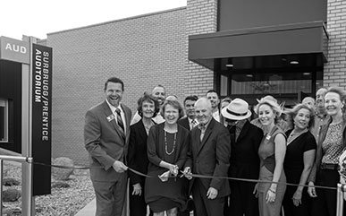 photo of the ribbon cutting for the Surbrugg/Prentice Auditorium with a crowd of people in front of the building. The college President Joe Schaffer and Dr. Surbrugg and Dr. Prentice are both cutting a ribbon.