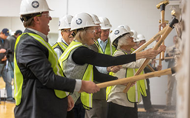 photo of President Joe Schaffer, the Board of Trustees and and special guests break ground – or in this case drywall