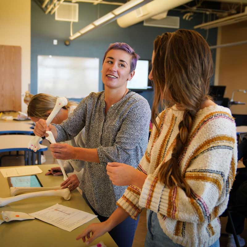 Science instructor talking with a student in class holding some leg bones