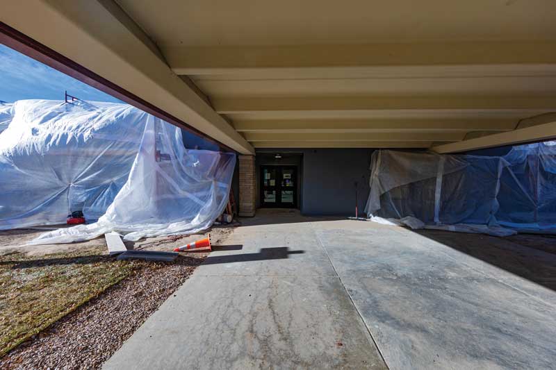 view of a building entryway under construction with side of the building draped in plastic