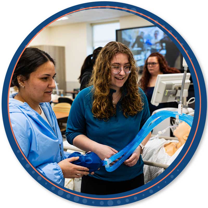 Two respiratory therapy students working with a respirator with tubes and a computer