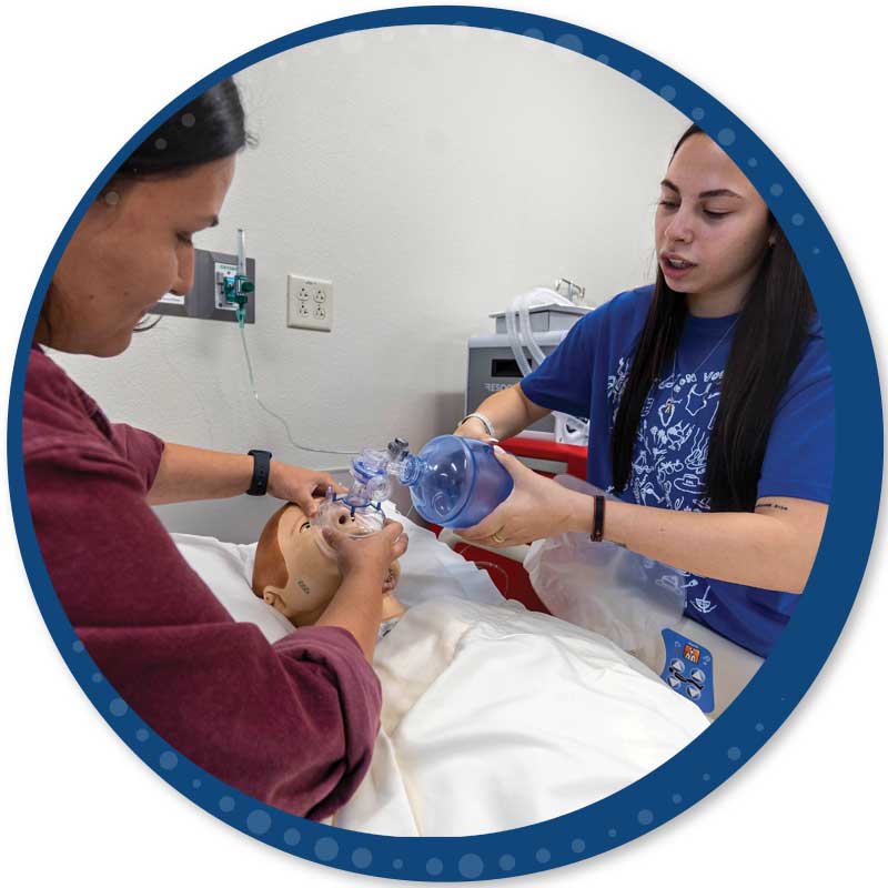 Two respiratory therapy students working on a patient simulator with a hand pump respirator