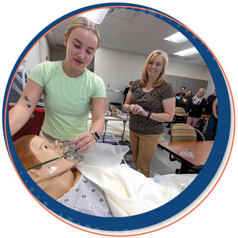 A respiratory therapy students working on a patient simulator with mask for oxygen as an instructor looks on