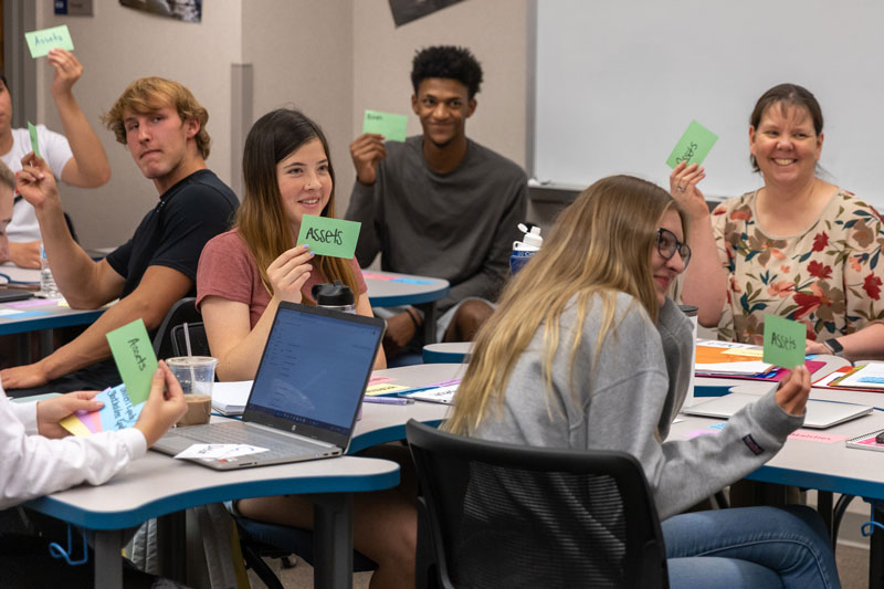 Photo of students in an accounting class holding up notecards that say "assets".