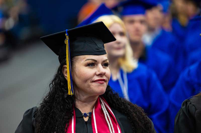 Jennifer Lamblin sitting at the commencement ceremony in her cap and gown
