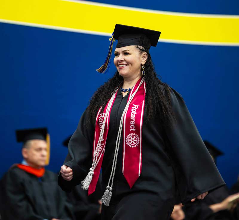 Jennifer Lamblin walking across the stage at commencement in cap and gown