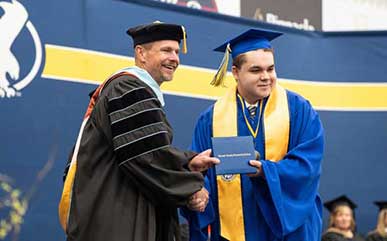 Caius Krupp shaking hands with Dr. Schaffer on stage during commencement