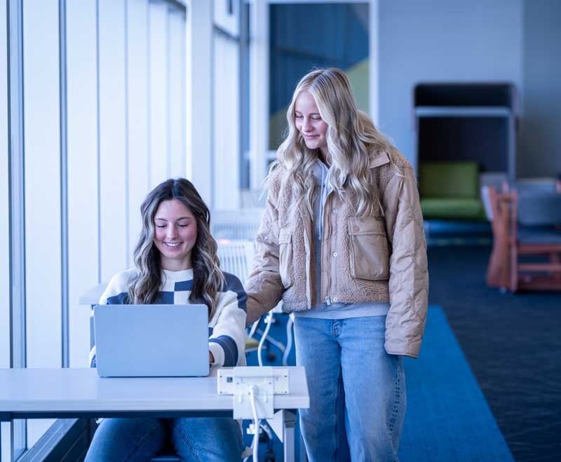 Two students in the library looking at a laptop.