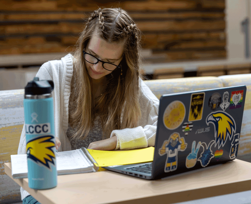 photo of student sitting at table with laptop, notepad and waterbottle