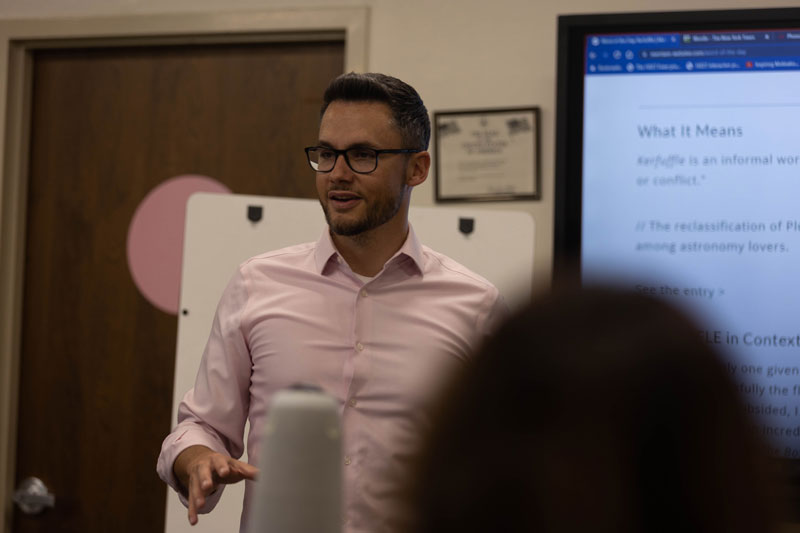 Photo of ESL instructor talking to class in front of a large screen with "what does it mean" written on it.