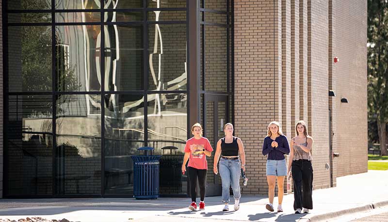 four students walking on campus in front of the Surbrugg/Prentice Auditorium