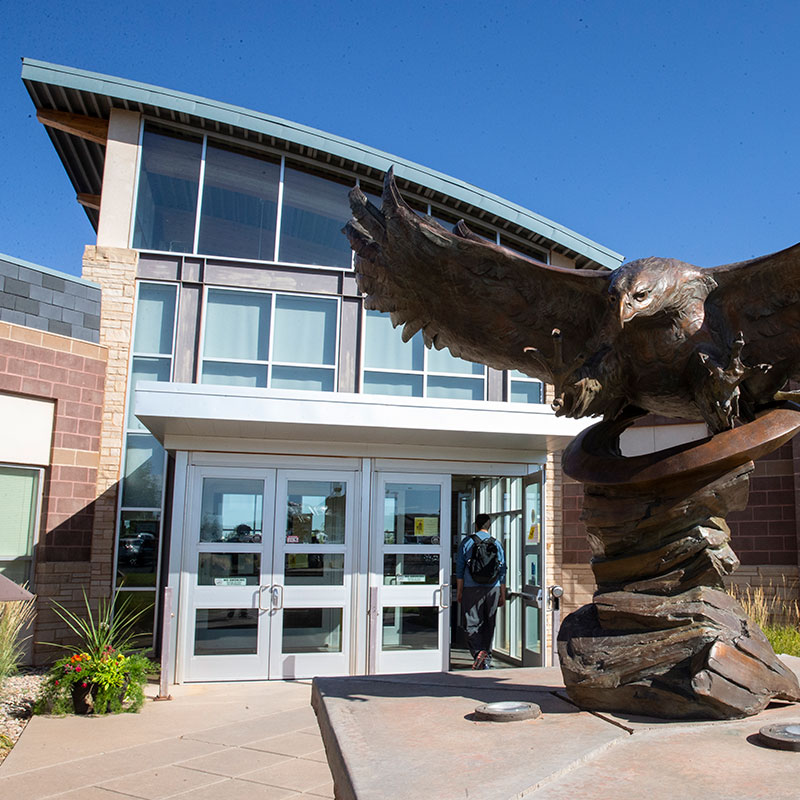 photo of the front of the ACC building with the eagle sculpture and the front doors. A male student is walking in the doors.
