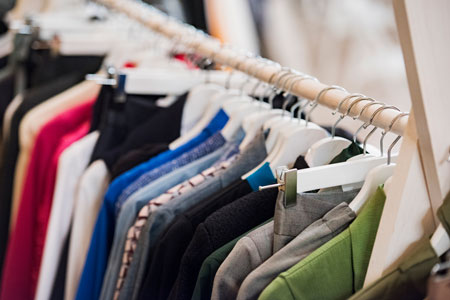 Photo of a rack of clothing hanging on hangers with tops and pants.