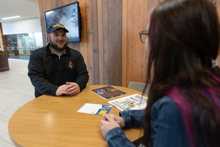 Photo of student body president Raeth Tolman sitting at a table across from another person in the Clay Pathfinder lobby.