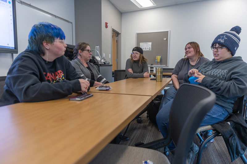 Photo of several students seated around a table talking. They are at a SAFE club meeting on campus.