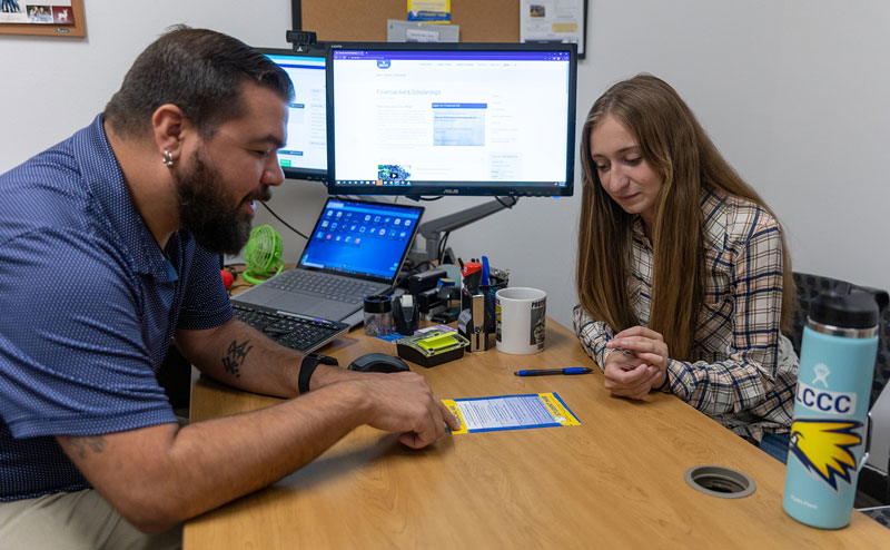 photo of LCCC advisor talking to female student in office. They are looking at information on a printed page with computer screens in the background.