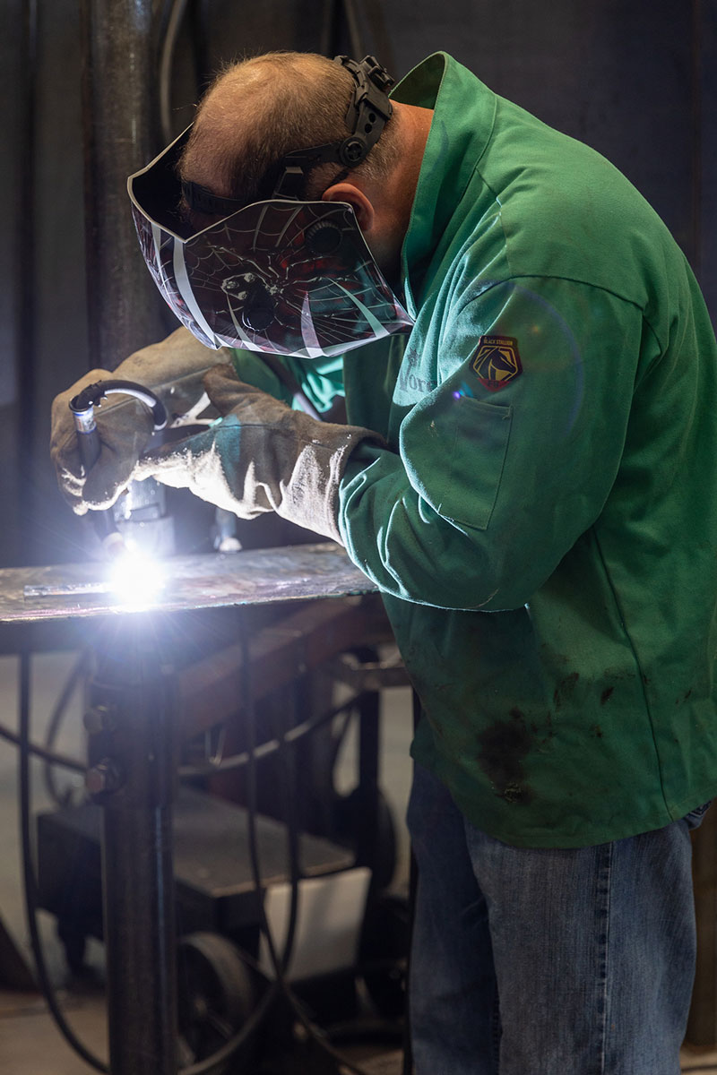 photo of male teacher welding in protective gear with sparks visible