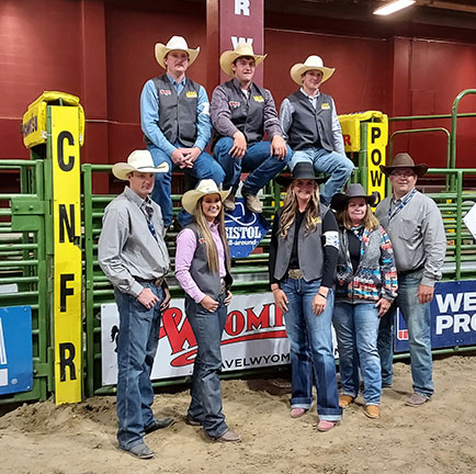 photo of LCCC's student participants and coaches at the College National Finals Rodeo grouped together on one of the gates for the bull/horse stalls.