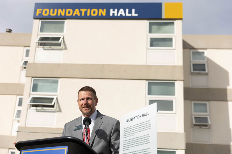 photo of LCCC President Joe Schaffer speaking at a poduim outside in front of Foundation Hall. The residence hall is visible in the background.