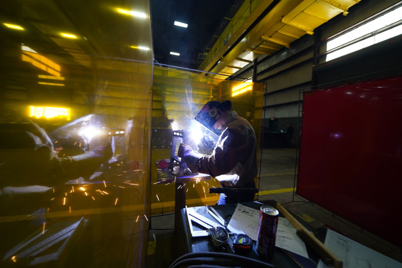 High school student welding at Puma Steel in welding competition wearing the protective helmet, coat and gloves.