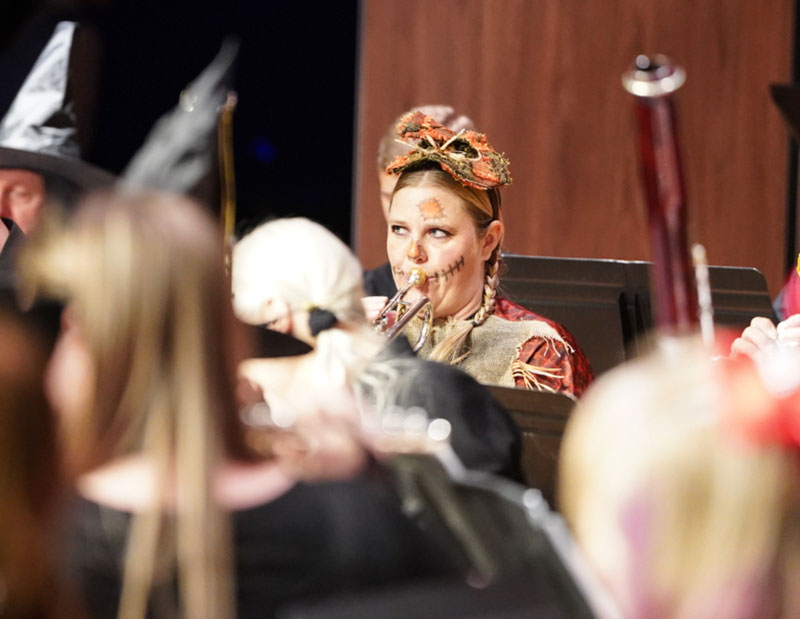 photo of a woman dressed as a scarecrow for Halloween playing a trumpet on stage during the concert