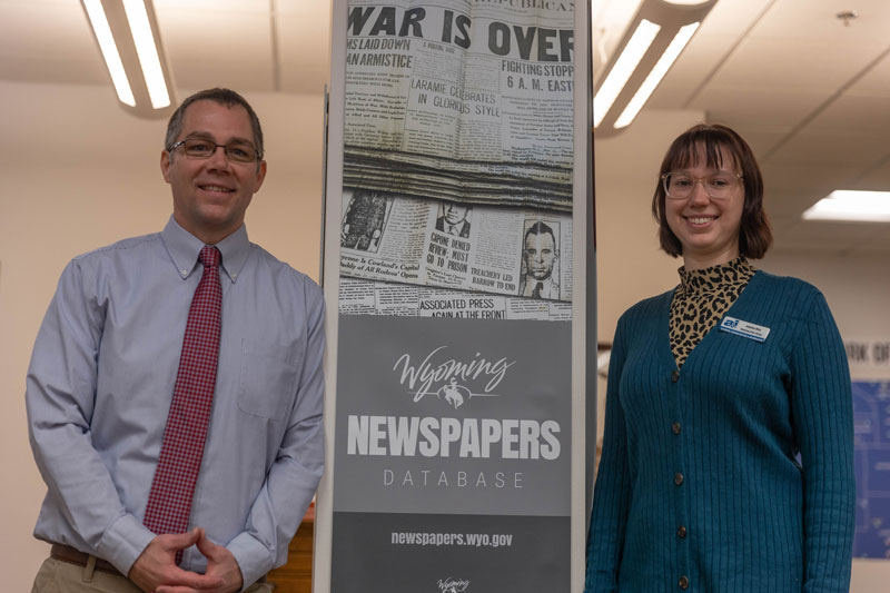 photo of two people standing next to a tall banner about a newspaper digital database