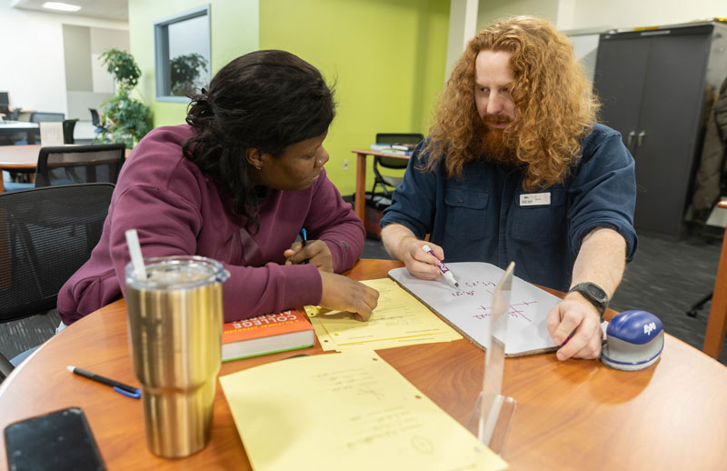 photo of Learning Commons tutor and student sitting at a table with books and talking