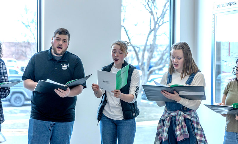 Photo of three choir members singing at an event in the lobby of the auditorium