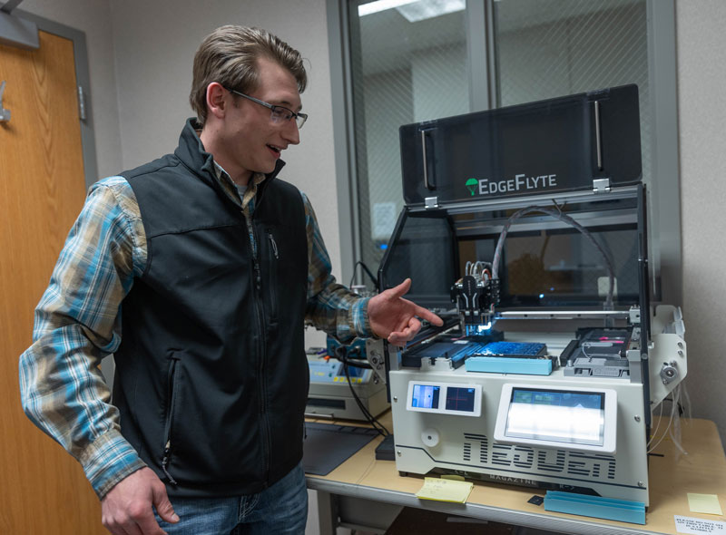 Tate Schrock pointing at a machine in the Entrepreneurship Lab