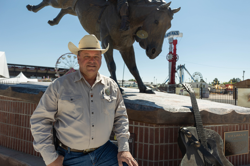 Bill Zink in front of a bull statue and the carnival at Cheyenne Frontier Days