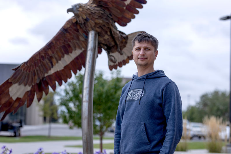 Sergei Cherepanov standing in front of eagle sculpture at LCCC