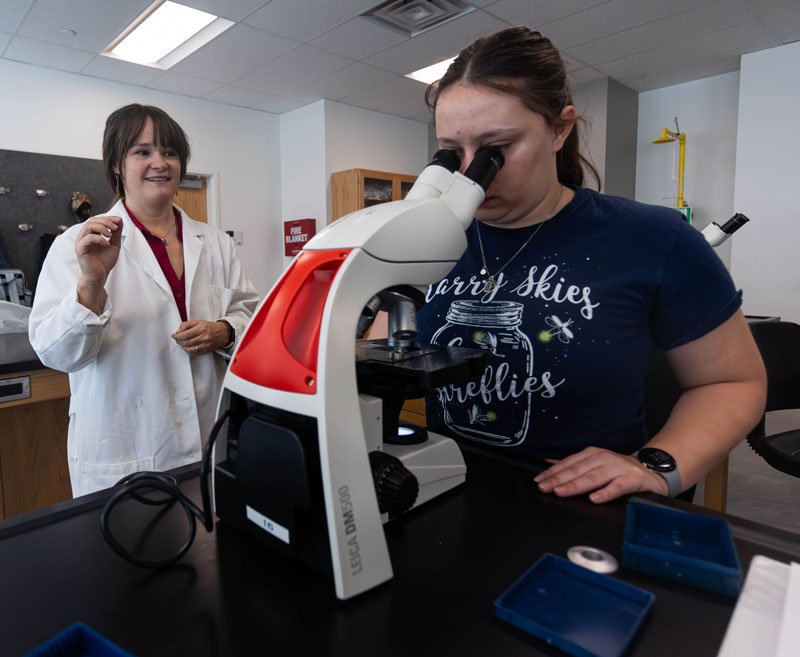 photo of Dr. Marie Yearling talking to a student looking into a microscope