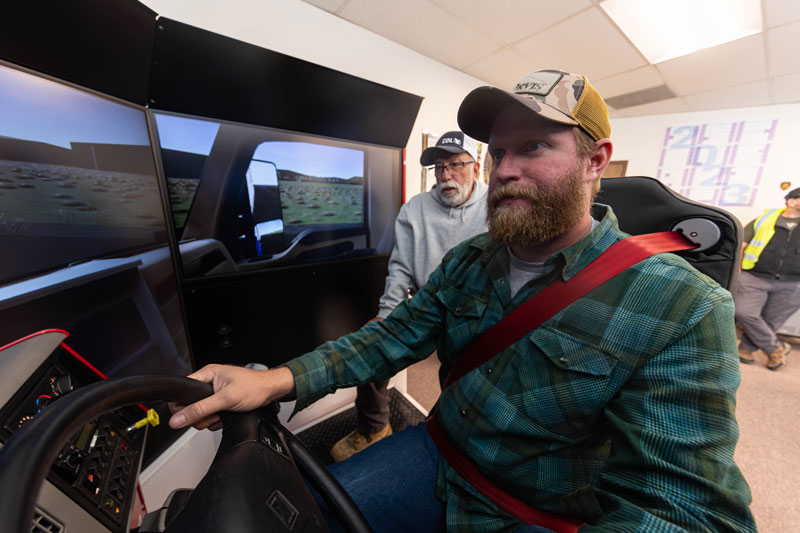 Photo of a student using the CDL driving simulator with an instructor standing behind them.