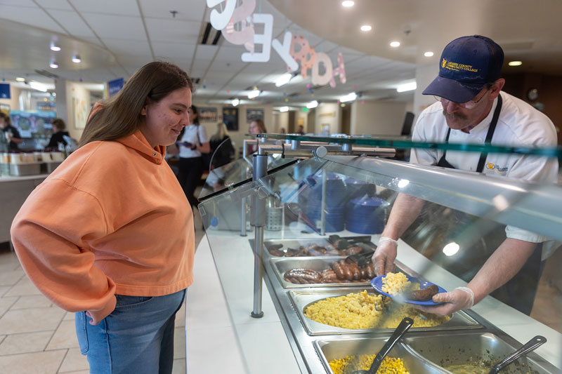 female student in the dining hall being served food from dining hall staff