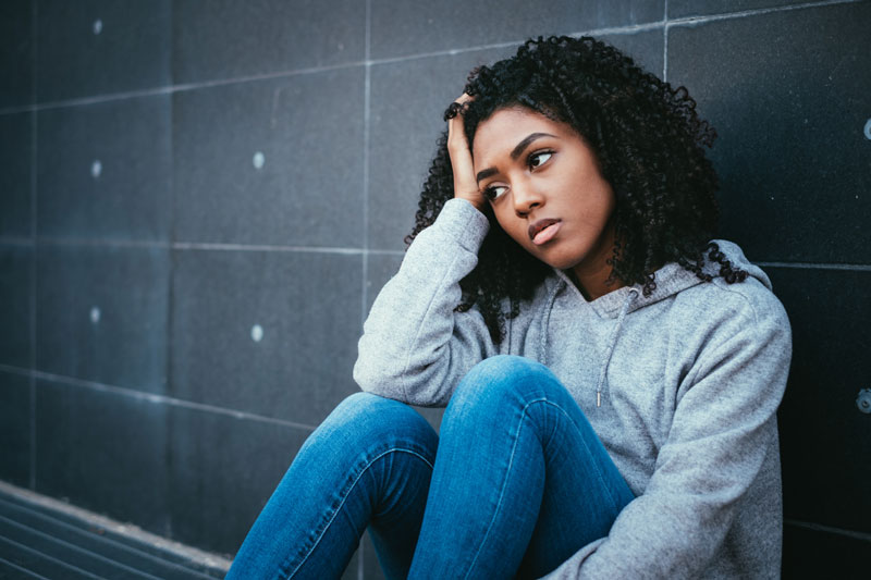 photo of a girl sitting against a wall leaning her head in her hand