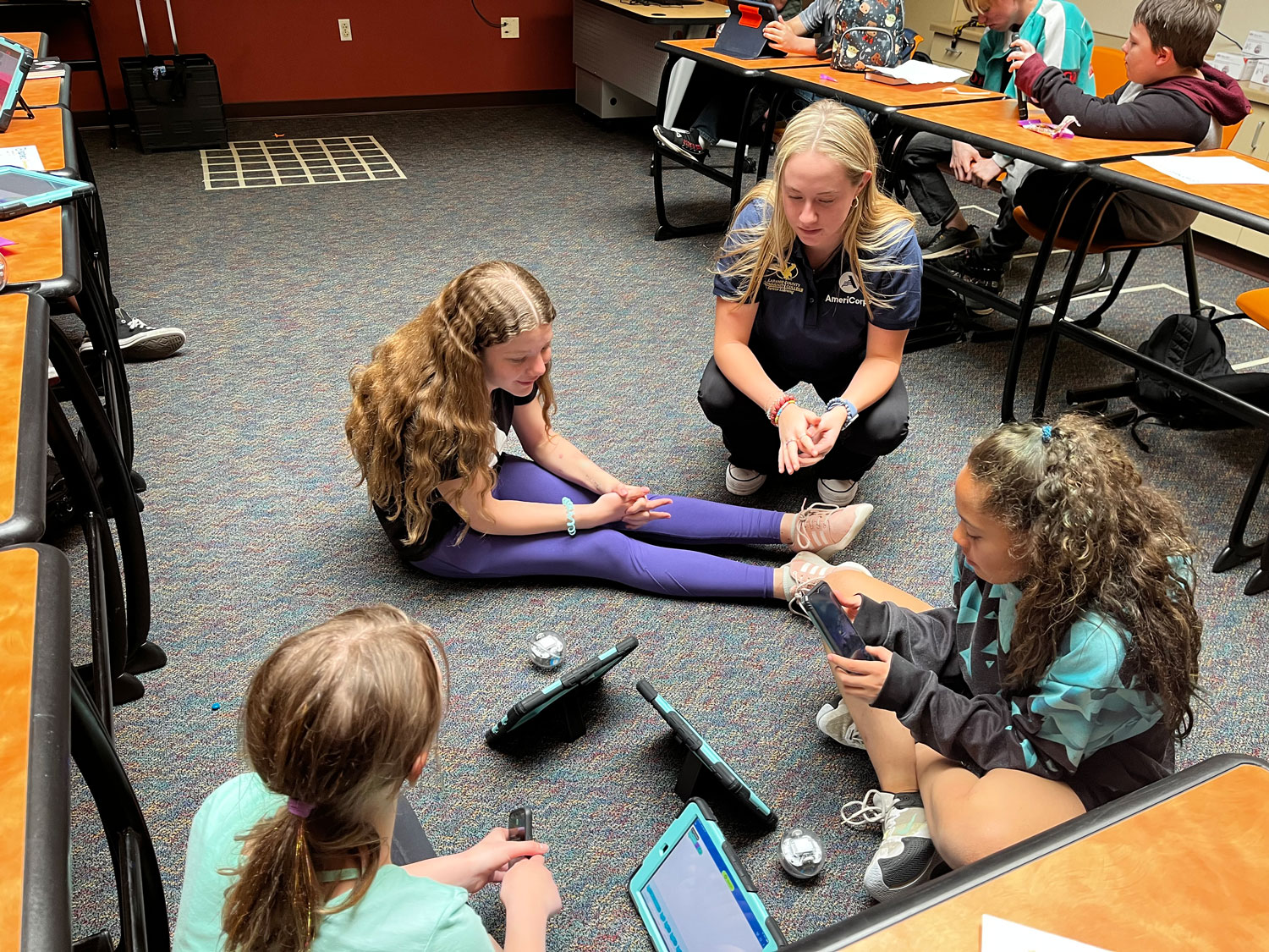photo of an LCCC student helping younger students with iPads while sitting on the floor