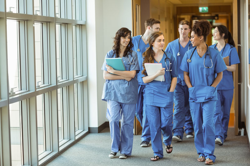 photo of a group of nursing students wearing scrubs and stethoscopes walking in a group down a hallway