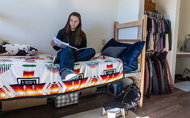 Photo of student sitting on bed in residence hall