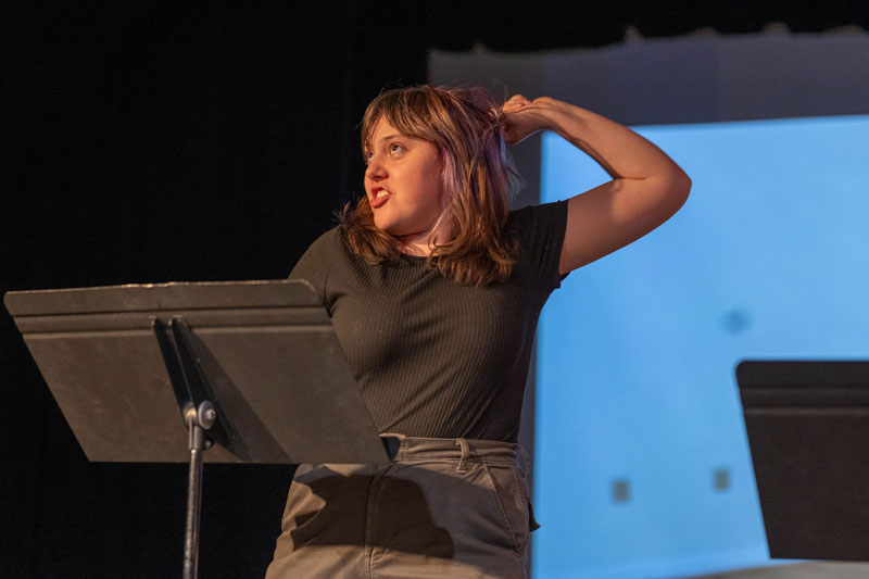 Photo of a student acting on stage with a music stand in front of her.
