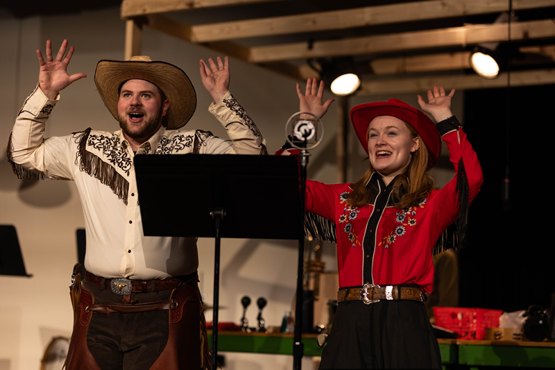 Photo of the CHAPS rehearsal with two actors dressed in cowboy gear raising their hands while singing.