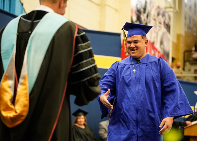 photo of an LCCC graduate walking across the stage in cap and gown to shake the LCCC President's hand.