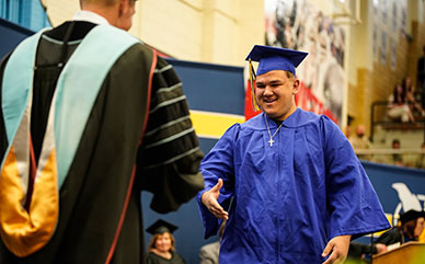 photo of an LCCC graduate walking across the stage in a cap and gown to shake hands with the LCCC President.