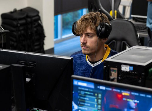 photo of an esports player at a computer with headphones on and his jersey.